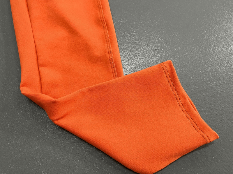 Bright orange leggings hem on a gray background, showcasing seamless stitching and vibrant fabric.